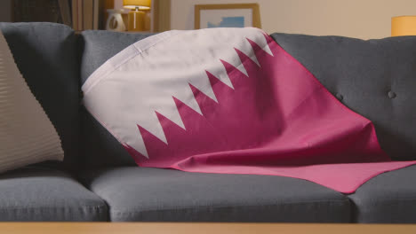 Flag-Of-Qatar-Draped-Over-Sofa-At-Home-Ready-For-Match-On-TV