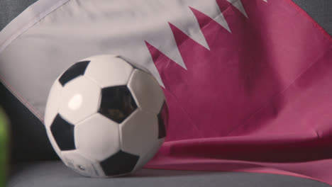 Flagge-Von-Katar-Drapiert-über-Dem-Sofa-Zu-Hause-Mit-Fußball-Bereit-Für-Das-Spiel-Im-Fernsehen