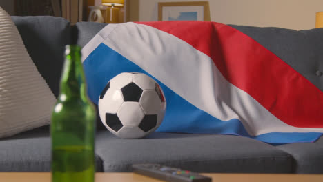 Flagge-Von-Holland-Drapiert-über-Dem-Sofa-Zu-Hause-Mit-Fußball-Bereit-Für-Das-Spiel-Im-Fernsehen