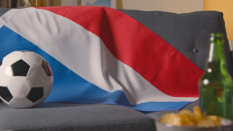 Flagge-Von-Holland-über-Dem-Sofa-Zu-Hause-Mit-Fußball-Bereit-Für-Das-Spiel-Im-Tv-1