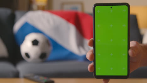 Green-Screen-Handy-Mit-Niederländischer-Flagge,-Die-Zu-Hause-über-Dem-Sofa-Drapiert-Ist,-Bereit-Für-Ein-Fußballspiel