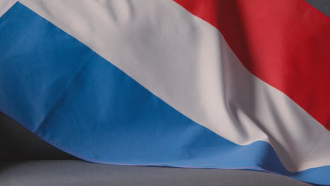 Primer-Plano-De-La-Bandera-De-Holanda-Sobre-Un-Sofá-En-Casa-Con-Fútbol-Listo-Para-El-Partido-En-La-Televisión