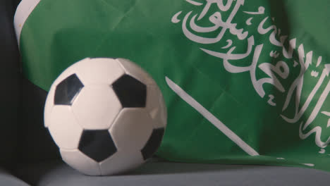Nahaufnahme-Der-Flagge-Von-Saudi-arabien,-Die-Zu-Hause-über-Dem-Sofa-Drapiert-Ist,-Mit-Dem-Fußball,-Der-Für-Das-Spiel-Im-Fernsehen-Bereit-Ist