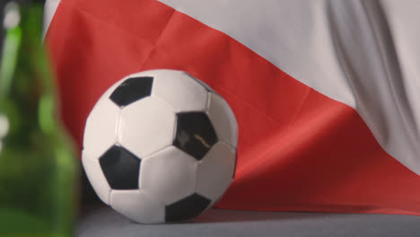 Flag-Of-Poland-Draped-Over-Sofa-At-Home-With-Football-Ready-For-Match-On-TV-2