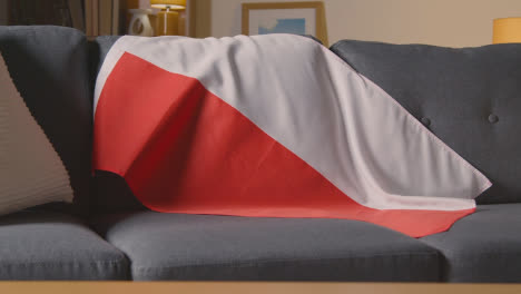 Flag-Of-Poland-Draped-Over-Sofa-At-Home-With-Football-Ready-For-Match-On-TV