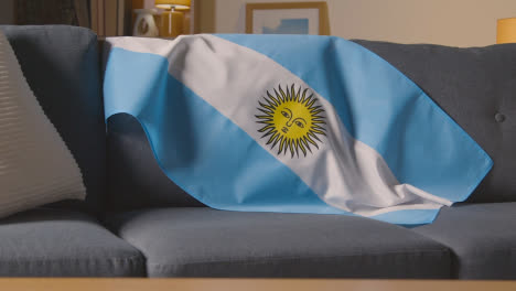 Flagge-Von-Argentinien-Drapiert-über-Sofa-Zu-Hause-Mit-Fußball-Bereit-Für-Spiel-Im-Fernsehen