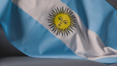 Nahaufnahme-Der-Flagge-Argentiniens,-Die-Zu-Hause-über-Dem-Sofa-Drapiert-Ist,-Mit-Dem-Fußball,-Der-Für-Das-Spiel-Im-Fernsehen-Bereit-Ist