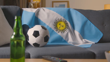 Flagge-Von-Argentinien-Drapiert-über-Sofa-Zu-Hause-Mit-Fußball-Bereit-Für-Spiel-Im-Fernsehen