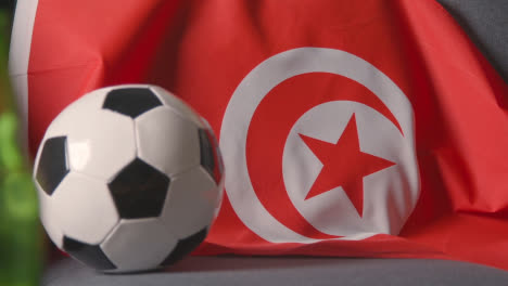 Flag-Of-Tunisia-Draped-Over-Sofa-At-Home-With-Football-Ready-For-Match-On-TV