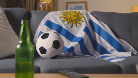 Flagge-Von-Uruguay-Drapiert-über-Dem-Sofa-Zu-Hause-Mit-Fußball-Bereit-Für-Das-Spiel-Im-Fernsehen
