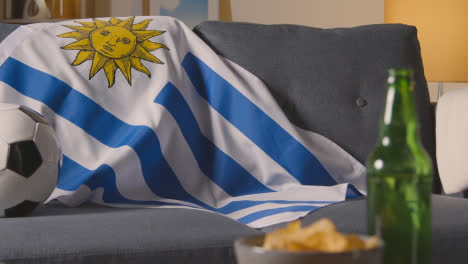 Flag-Of-Uruguay-Draped-Over-Sofa-At-Home-With-Football-Ready-For-Match-On-TV-1