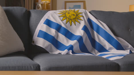 Flag-Of-Uruguay-Draped-Over-Sofa-At-Home-Ready-For-Match-On-TV