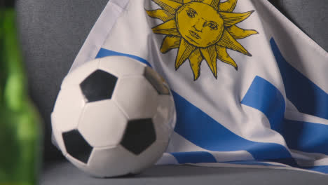 Flagge-Von-Uruguay-Zu-Hause-über-Sofa-Drapiert,-Fußball-Bereit-Für-Spiel-Im-Tv-2