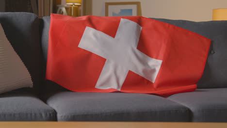 Flag-Of-Switzerland-Draped-Over-Sofa-At-Home-Ready-For-Match-On-TV
