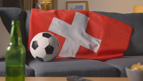 Flagge-Der-Schweiz-Zu-Hause-über-Dem-Sofa-Drapiert,-Fußball-Bereit-Für-Das-Spiel-Im-Fernsehen