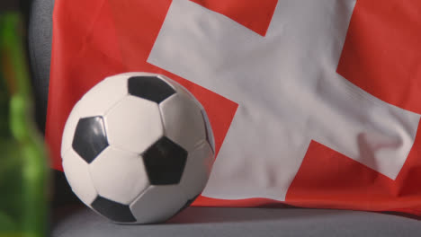 Flagge-Der-Schweiz-Zu-Hause-über-Sofa-Drapiert,-Fußball-Bereit-Für-Spiel-Im-Tv-2