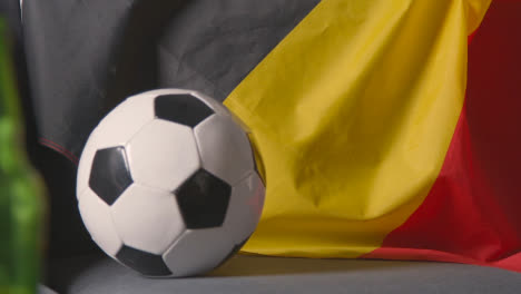 Flagge-Von-Belgien-Drapiert-über-Dem-Sofa-Zu-Hause-Mit-Fußball-Bereit-Für-Das-Spiel-Im-Fernsehen
