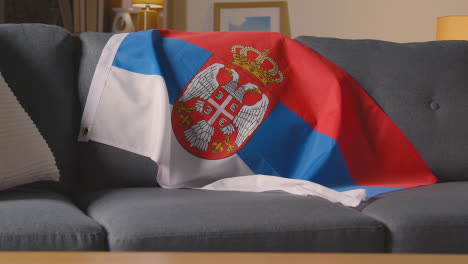Flag-Of-Serbia-Draped-Over-Sofa-At-Home-Ready-For-Match-On-TV