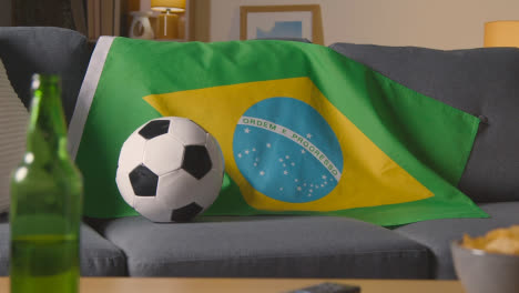 Flagge-Von-Brasilien-Drapiert-über-Dem-Sofa-Zu-Hause-Mit-Fußball-Bereit-Für-Das-Spiel-Im-Fernsehen