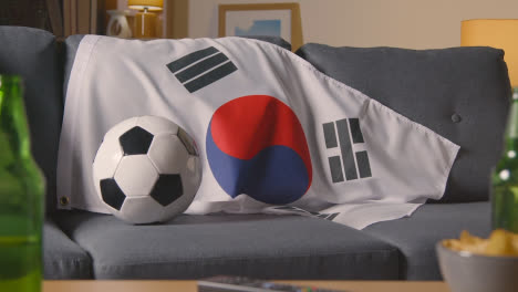 Die-Flagge-Südkoreas-Liegt-Zu-Hause-über-Dem-Sofa,-Während-Der-Fußball-Für-Das-Spiel-Im-Fernsehen-Bereit-Ist
