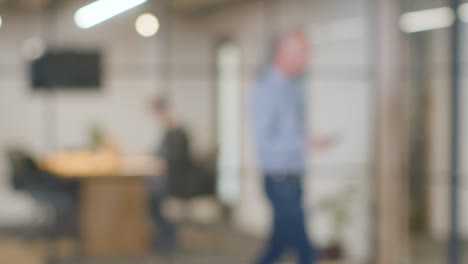 Defocused-Background-Shot-Of-Businesspeople-Working-At-Desk-In-Office-And-Talking-On-Phone