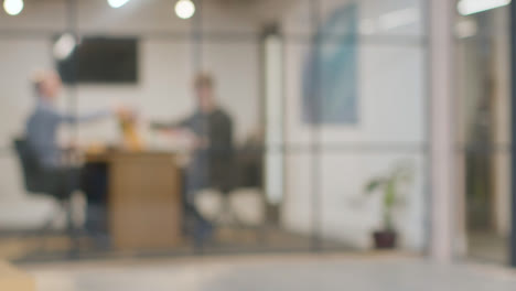 Defocused-Background-Shot-Of-Businesspeople-At-Work-In-Office-Having-Meeting-At-Desk