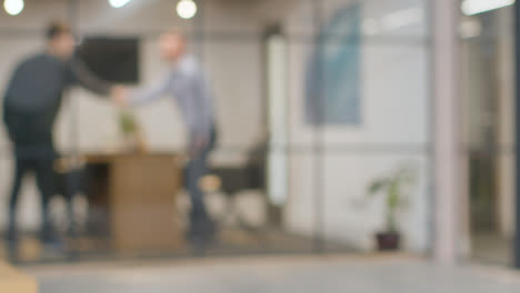 Defocused-Background-Shot-Of-Businesspeople-At-Work-In-Office-Shaking-Hands-Before-Meeting-At-Desk-