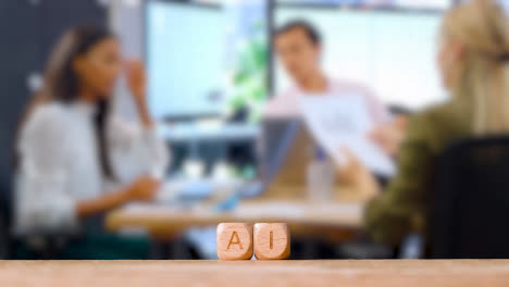 Business-Concept-Wooden-Letter-Cubes-Or-Dice-Spelling-AI-With-Office-Meeting-In-Background