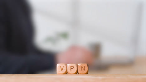 Geschäftskonzept-Hölzerne-Buchstabenwürfel-Oder-Würfel,-Die-Vpn-Buchstabieren,-Mit-Büroangestellten,-Die-Im-Hintergrund-Am-Laptop-Arbeiten