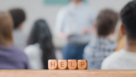 Education-Concept-With-Wooden-Letter-Cubes-Or-Dice-Spelling-Help-With-Student-Lecture-In-Background