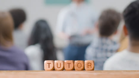 Education-Concept-With-Wooden-Letter-Cubes-Or-Dice-Spelling-Tutor-With-Student-Lecture-In-Background