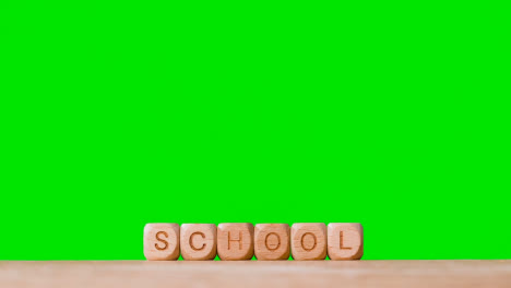 Education-Concept-With-Wooden-Letter-Cubes-Or-Dice-Spelling-School-Against-Green-Screen