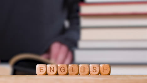 Education-Concept-Shot-With-Wooden-Letter-Cubes-Or-Dice-Spelling-English-With-Person-Reading-Book-In-Library