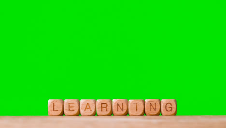 Education-Concept-With-Wooden-Letter-Cubes-Or-Dice-Spelling-Learning-Against-Green-Screen