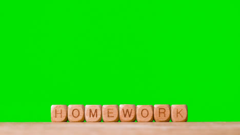 Education-Concept-With-Wooden-Letter-Cubes-Or-Dice-Spelling-Homework-Against-Green-Screen