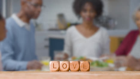 Concept-With-Wooden-Letter-Cubes-Or-Dice-Spelling-Love-Against-Background-Of-Family-Eating-Meal-At-Home
