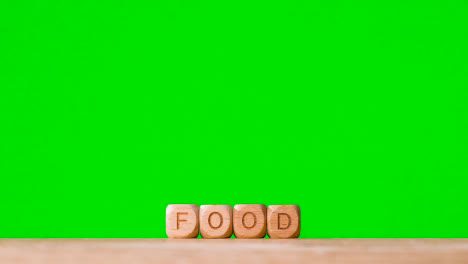 Konzept-Mit-Hölzernen-Buchstabenwürfeln-Oder-Würfeln,-Die-Lebensmittel-Vor-Grünem-Hintergrund-Buchstabieren
