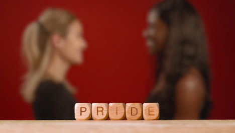 Concept-With-Wooden-Letter-Cubes-Or-Dice-Spelling-Pride-Against-Background-Of-Same-Sex-Female-Couple-Hugging