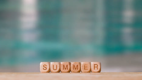 Concept-With-Wooden-Letter-Cubes-Or-Dice-Spelling-Summer-Against-Background-Of-Rippling-Water