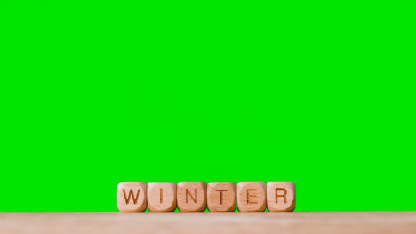 Konzept-Mit-Hölzernen-Buchstabenwürfeln-Oder-Würfeln,-Die-Winter-Vor-Grünem-Hintergrund-Buchstabieren