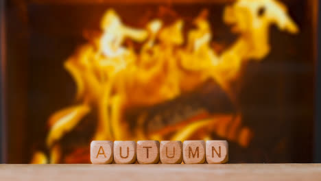 Concept-With-Wooden-Letter-Cubes-Or-Dice-Spelling-Autumn-Against-Background-Of-Blazing-Log-Fire