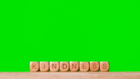 Concept-With-Wooden-Letter-Cubes-Or-Dice-Spelling-Kindness-Against-Green-Screen-Background