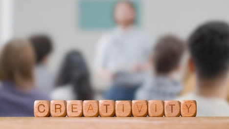 Concept-With-Wooden-Letter-Cubes-Or-Dice-Spelling-Creativity-Against-Background-Of-People-Meeting-To-Discuss-Ideas