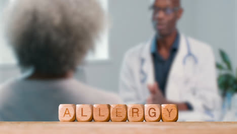 Medical-Concept-With-Wooden-Letter-Cubes-Or-Dice-Spelling-Allergy-Against-Background-Of-Doctor-Talking-To-Patient-In-Hospital