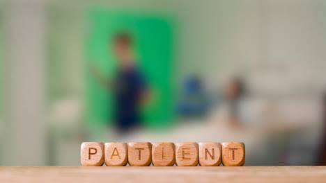 Medical-Concept-With-Wooden-Letter-Cubes-Or-Dice-Spelling-Patient-Against-Background-Of-Nurse-Talking-To-Patient-In-Hospital-Bed
