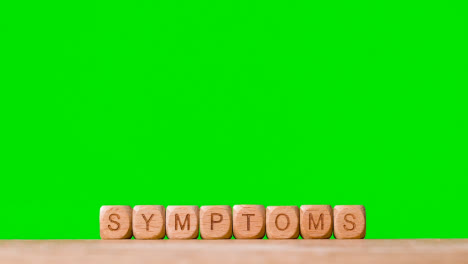 Medical-Concept-With-Wooden-Letter-Cubes-Or-Dice-Spelling-Symptoms-Against-Green-Screen-Background