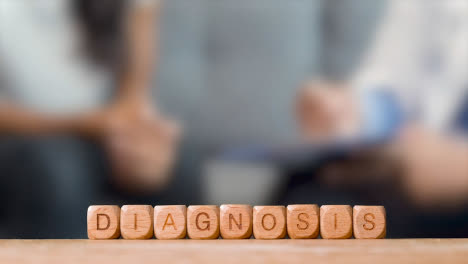 Medical-Concept-With-Wooden-Letter-Cubes-Or-Dice-Spelling-Diagnosis-Against-Background-Of-Doctor-Talking-To-Patient