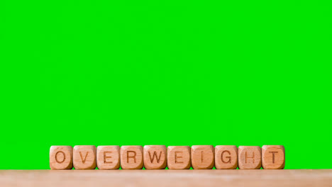 Medical-Concept-With-Wooden-Letter-Cubes-Or-Dice-Spelling-Overweight-Against-Green-Screen-Background