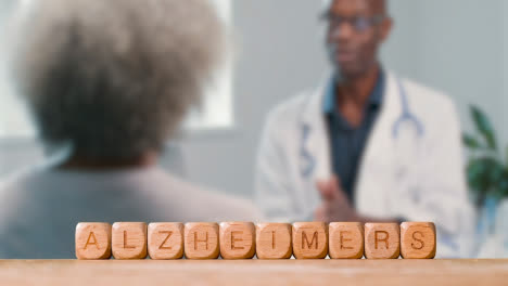 Medical-Concept-With-Wooden-Letter-Cubes-Or-Dice-Spelling-Alzheimer's-Against-Background-Of-Doctor-Talking-To-Patient
