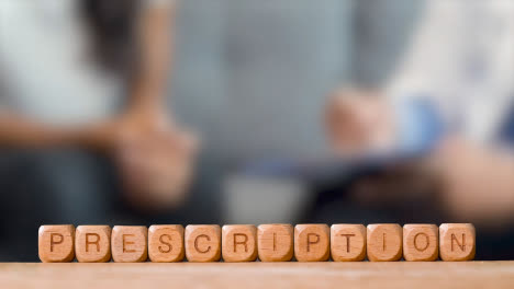 Medical-Concept-With-Wooden-Letter-Cubes-Or-Dice-Spelling-Prescription-Against-Background-Of-Doctor-Talking-To-Patient